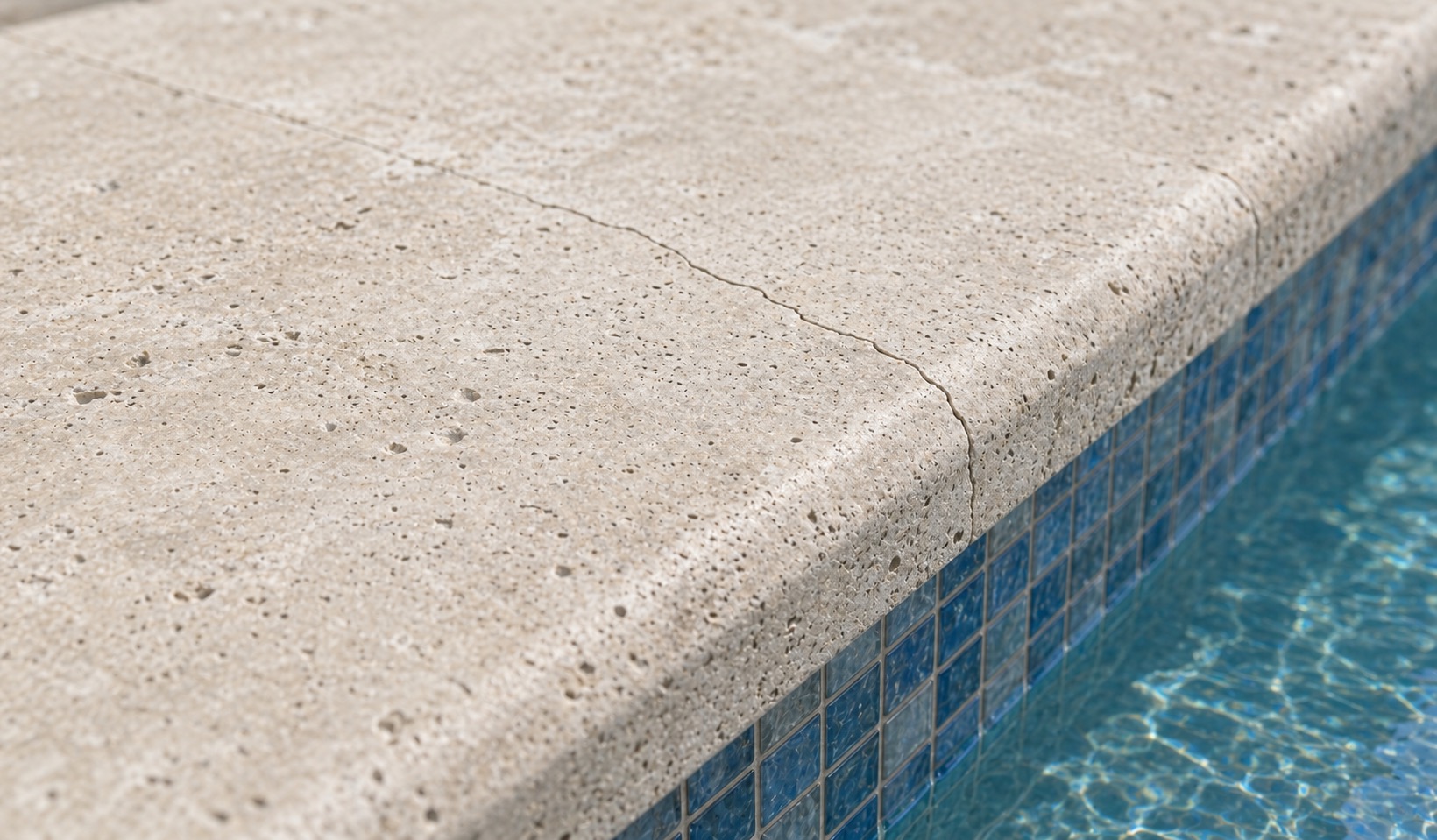 Close-up of a hairline crack crossing travertine coping near a pool edge