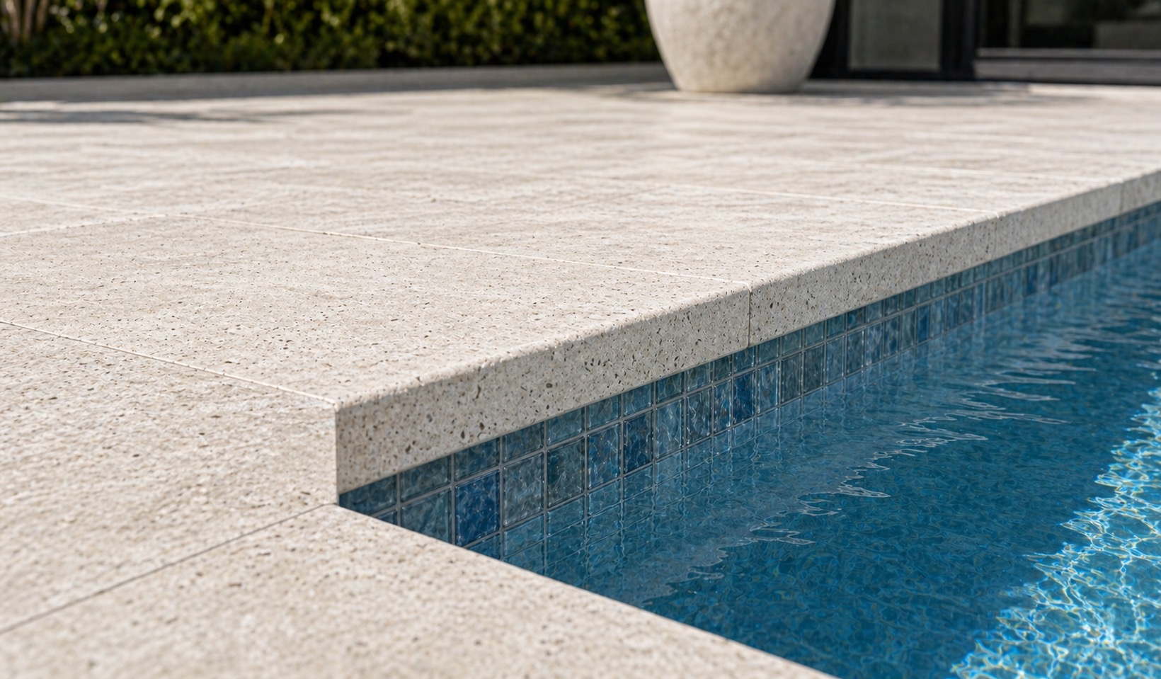 Close detail of straight-edge travertine coping meeting a pale modern pool deck